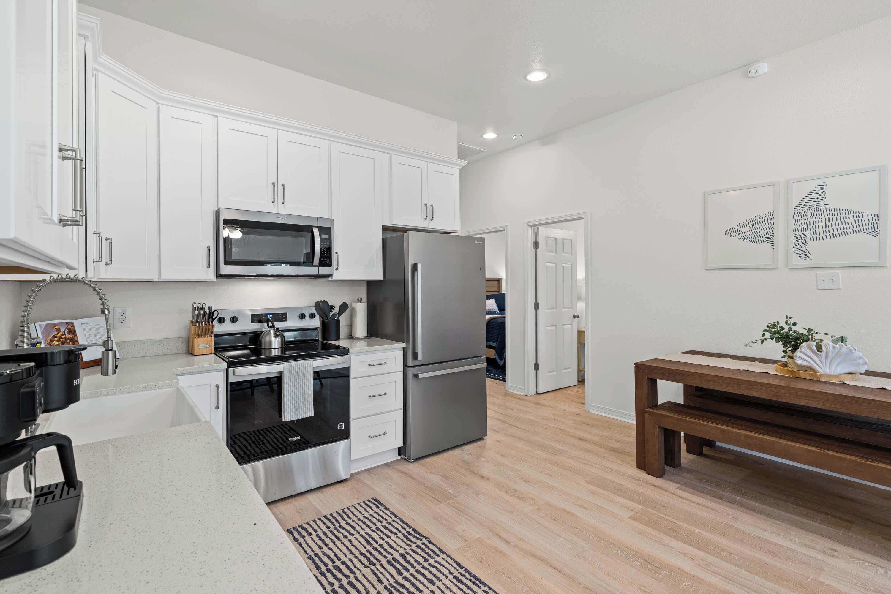 A modern kitchen with white cabinets, stainless steel appliances, a wooden bench, and two wall art pieces.