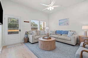 A living room with two sofas, a round coffee table, a ceiling fan, and a door with a view of the outdoors.