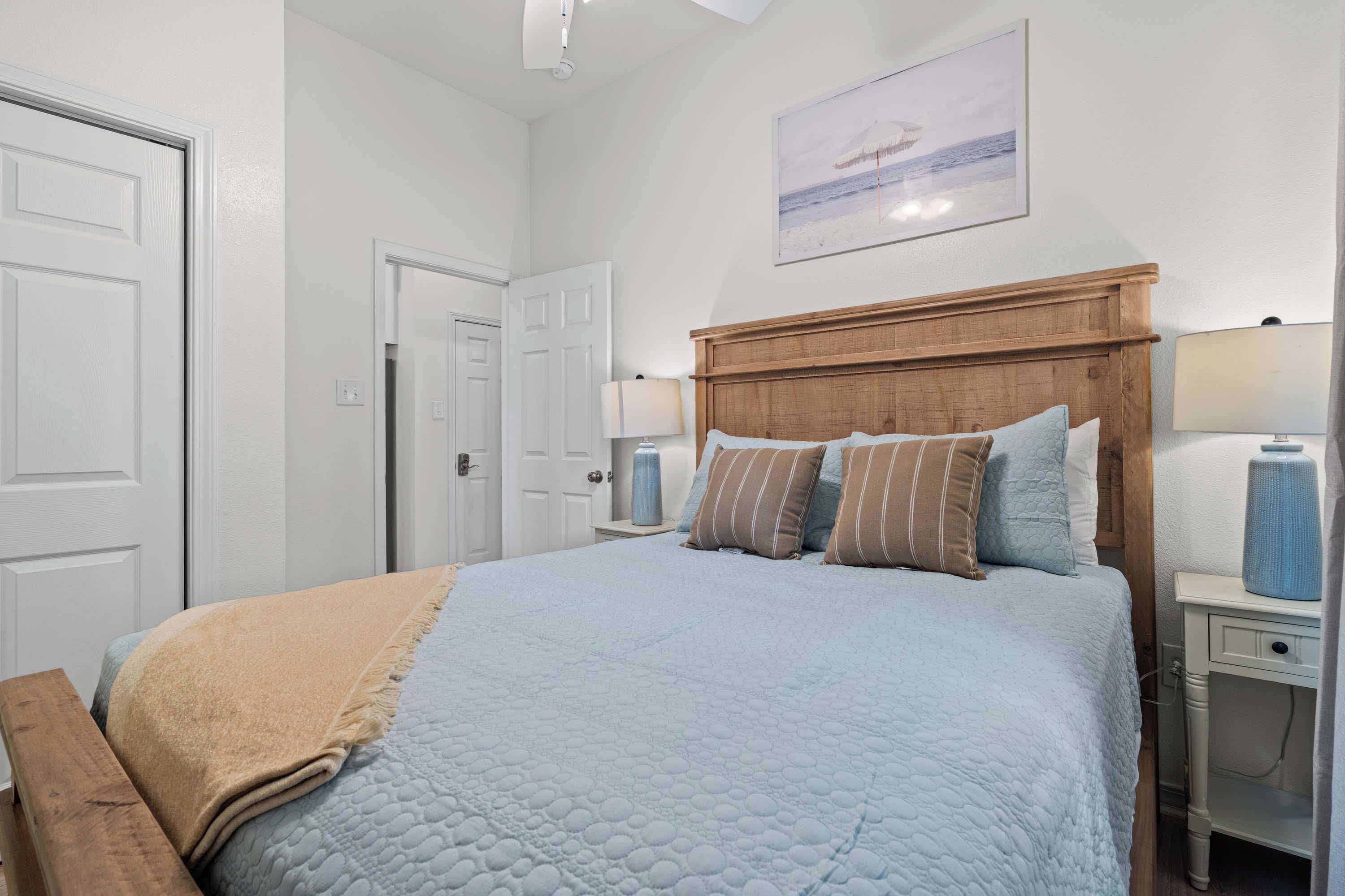 A bedroom with a bed, a wooden headboard, bedside tables with lamps, a door, and a framed picture on the wall.