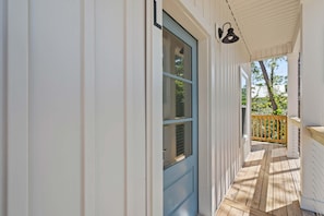 A covered porch with a blue door, wooden railing, and a view of greenery.