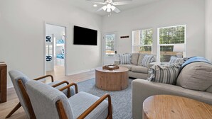 Un salon moderne doté d’un ventilateur de plafond, d’un téléviseur à écran plat, d’une table basse ronde en bois et d’un canapé avec des coussins à rayures.