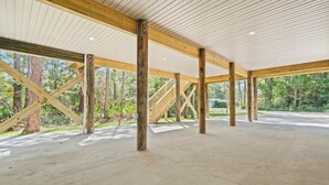 Un espace ouvert et vaste, avec des poutres en bois et un sol en béton, entouré d’arbres.