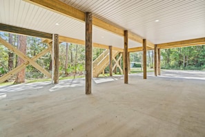 An open, spacious area with wooden beams and a concrete floor, surrounded by trees.