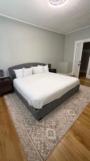 Ein Schlafzimmer mit einem großen Bett, einem Nachttisch, einer Lampe und einem gemusterten Teppich.