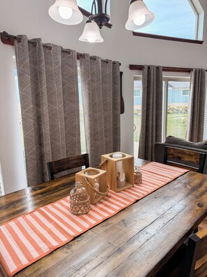Een houten eettafel met een geribbelde placemat, twee houten kandelaars met kaarsen, en een glazen fles met touwkoord.