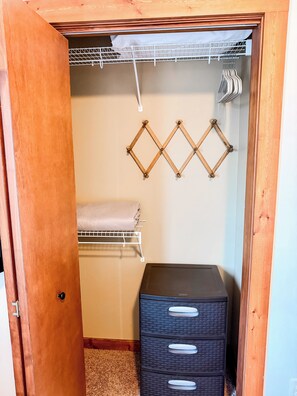 A wooden closet with a hanging rack, a folded towel, and a black storage unit.