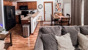 Een moderne keuken met houten kastjes, een zwarte koelkast, en een eethoek met een houten tafel en stoelen.