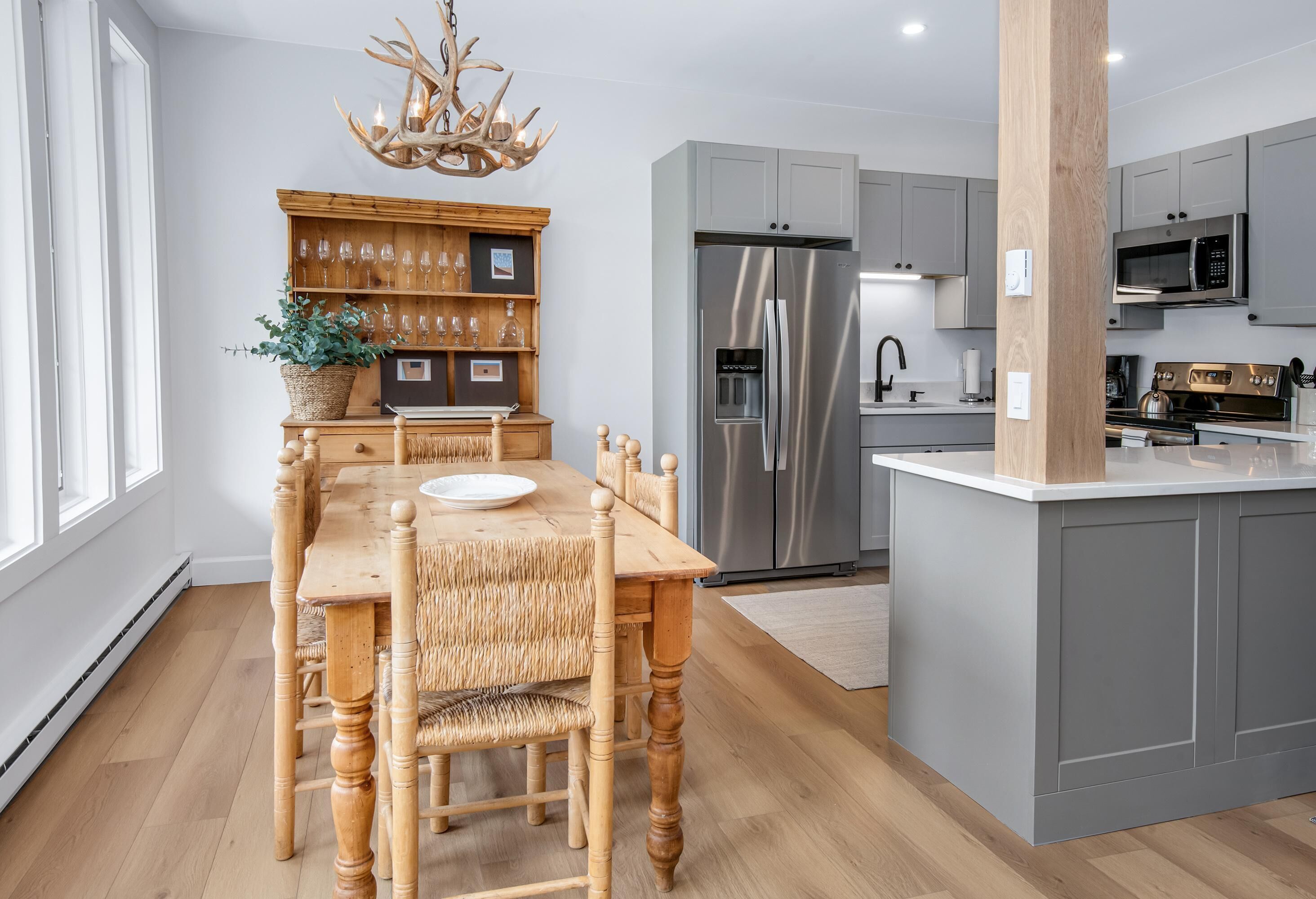 Une cuisine moderne avec des meubles gris, un réfrigérateur en acier inoxydable et un coin repas comprenant une table et des chaises en bois.