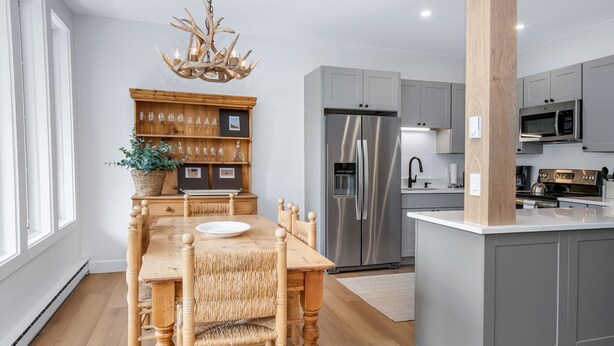Una cocina moderna con armarios grises, un refrigerador de acero inoxidable y un comedor con mesa y sillas de madera.