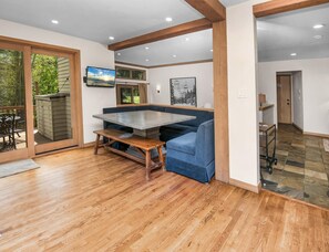 Ein modernes Interieur mit Holzboden, einem großen Tisch, blauem Sitzmöbel und Blick durch eine Glastür.