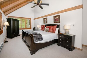 Ein Schlafzimmer mit einem großen Bett, einem Schminktisch, einem Nachttisch, einem Deckenventilator und einem Fenster mit Jalousien.