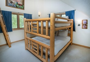 Un lit superposé avec une échelle, une fenêtre avec des rideaux et un luminaire fixé au mur.