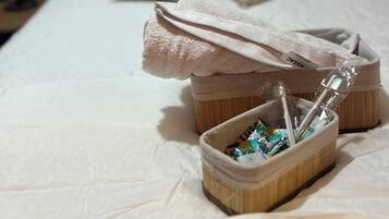 A neatly made bed with pillows, a small wooden basket with toiletries, and a folded towel on the bed.