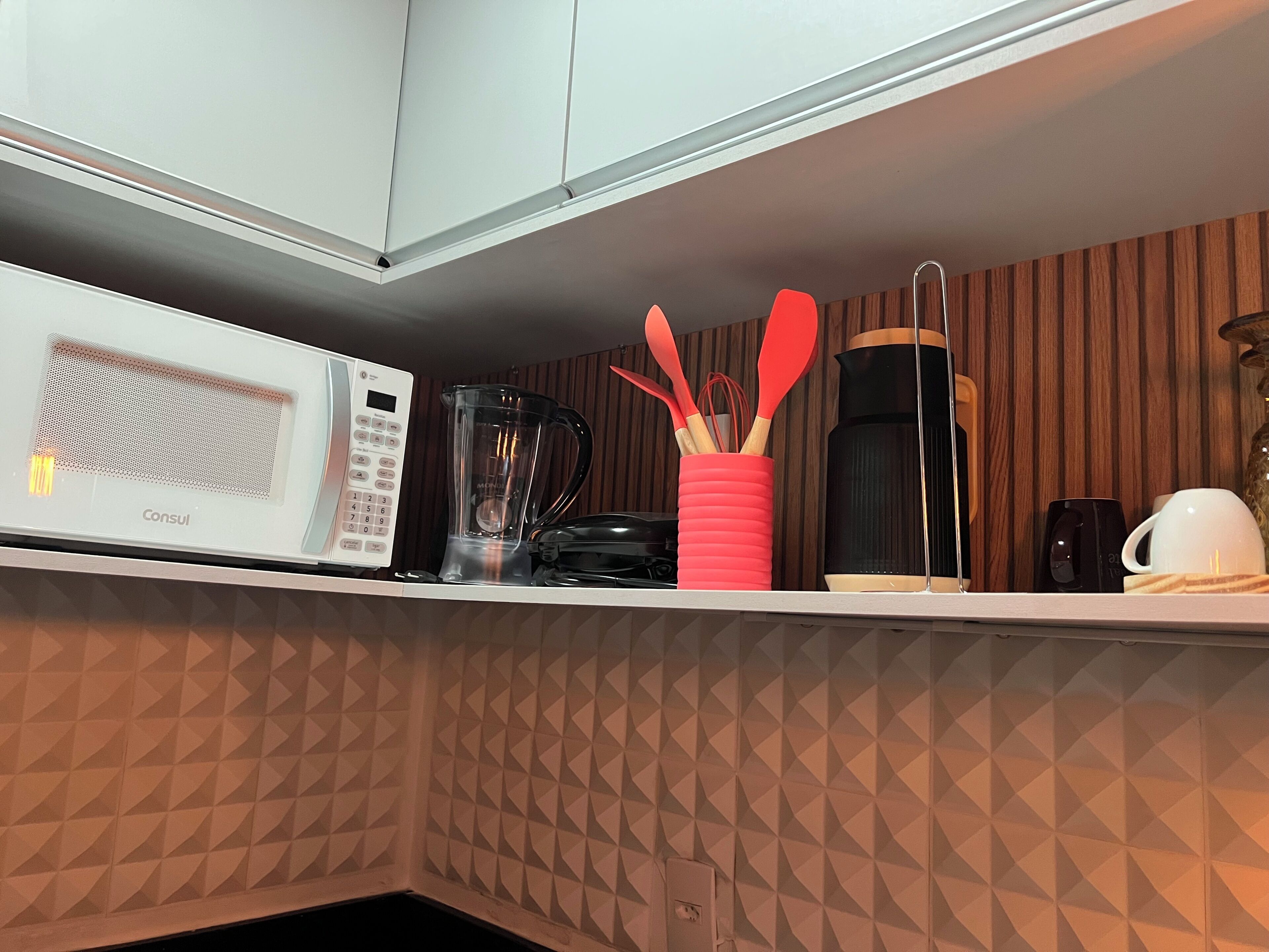 A kitchen with a microwave, blender, coffee maker, and utensils on the counter.