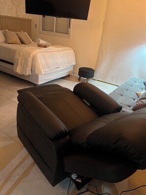 A modern bedroom with a bed, a sofa, a TV, and a small table. - Apartamento completo, próximo ao aeroporto de Guarulhos - Via alameda (Guarulhos)