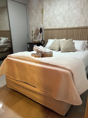 A neatly made bed with a quilt, a bedside table with a clock, and a mirror on the wall. - Apartamento completo, próximo ao aeroporto de Guarulhos - Via alameda (Guarulhos)