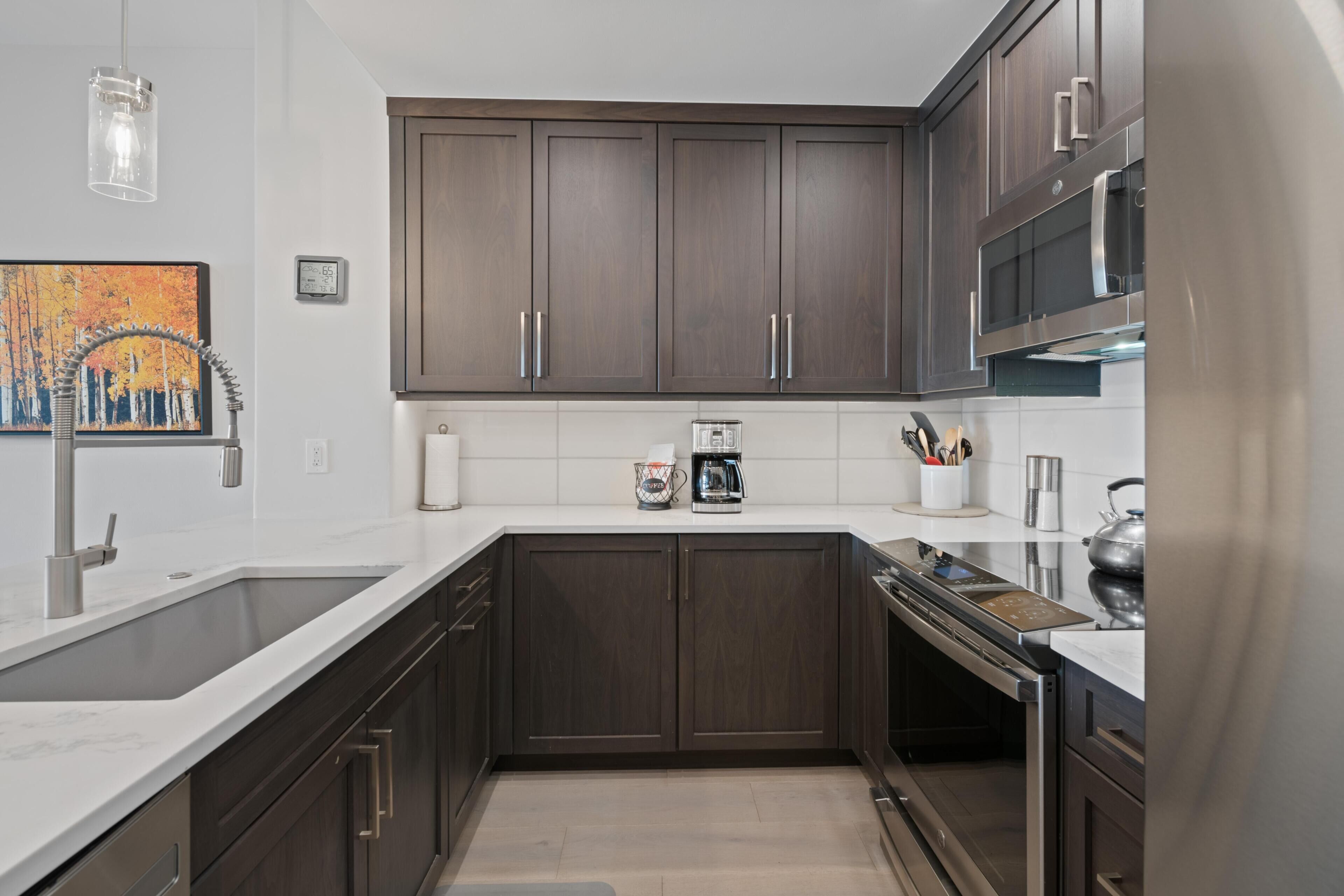 Una cocina moderna con armarios de madera oscura, electrodomésticos de acero inoxidable y una encimera blanca.