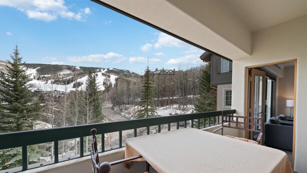 Ein Balkon mit Tisch und Stuhl mit Blick auf eine verschneite Berglandschaft.