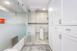 Un baño moderno con cabina de ducha de vidrio, muebles blancos y suelo de baldosas.
