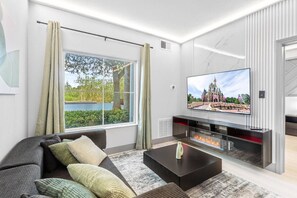 Ein modernes Wohnzimmer mit großem Fernseher, Kamin und Blick auf ein Schloss durch das Fenster.