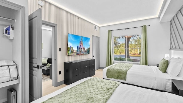 Ein modernes Hotelzimmer mit zwei Betten, einem Flachbildfernseher, einem großen Fenster mit Vorhängen und Blick auf ein Schloss.