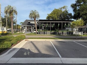 A building with a covered outdoor area, palm trees, and a parking lot.