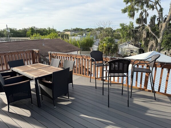 A deck with a table and chairs, overlooking a residential area with trees and houses.