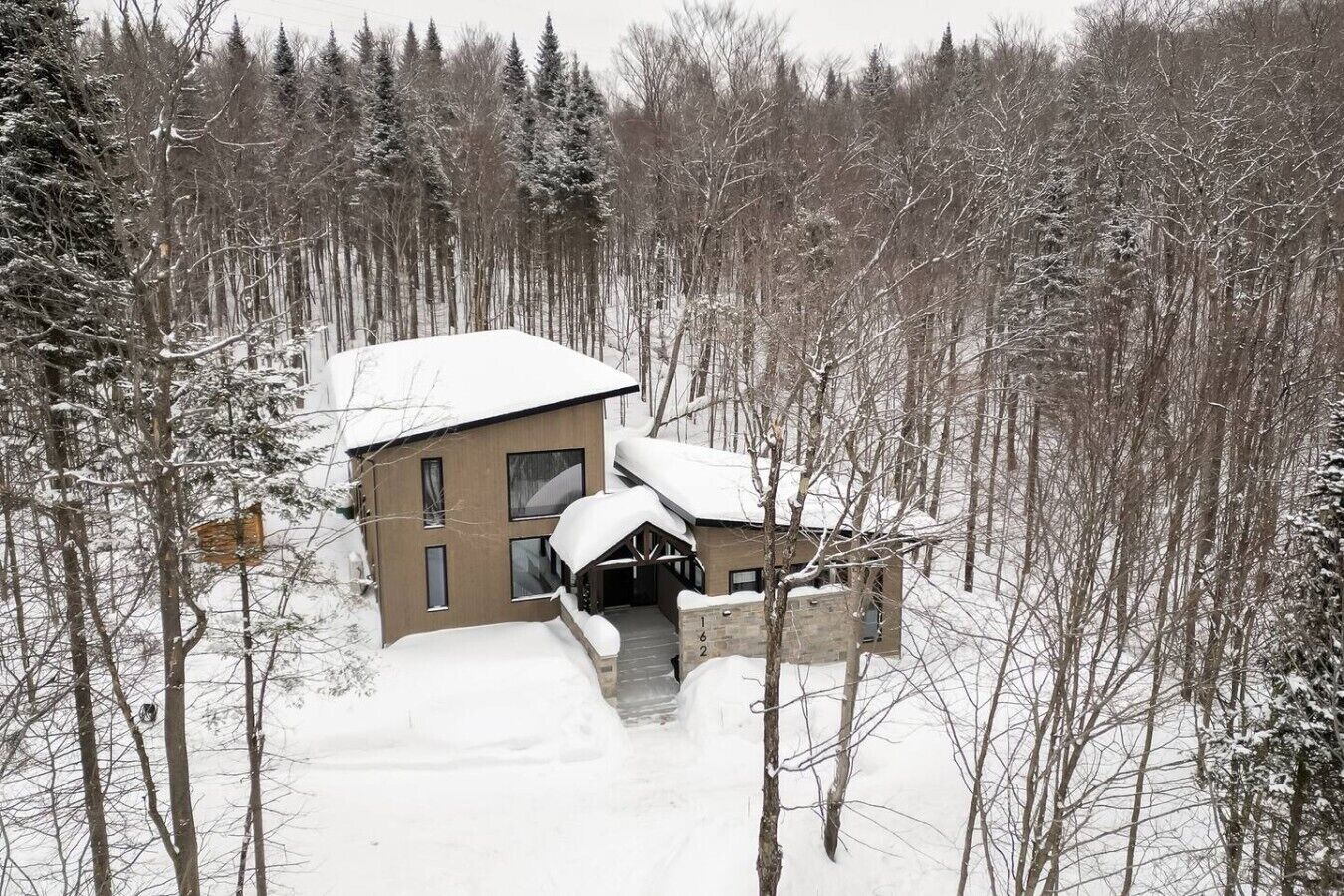 Un edificio de dos pisos con un techo cubierto de nieve, rodeado de un bosque.