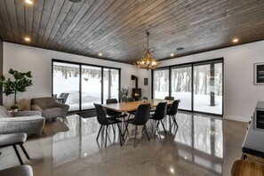 A modern interior with a wooden ceiling, large windows, a dining table, and black chairs. - Le Miléna | Private SPA & Sauna | Billiards & Pool (Les Laurentides Regional County Municipality)