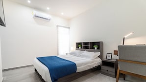 A modern bedroom with a bed, bedside tables, a chair, and an air conditioning unit. - Bella Terra (Hermosillo)