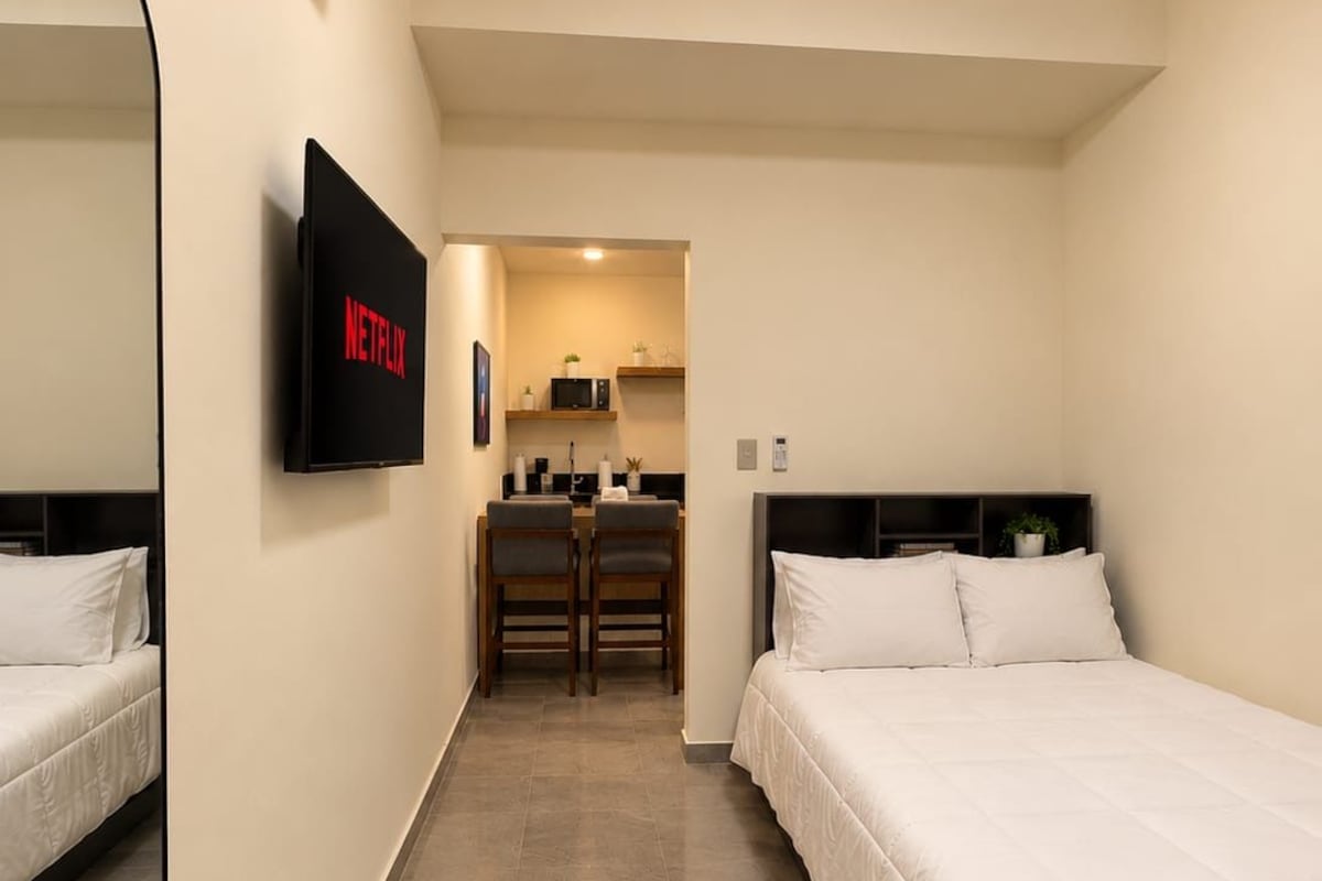 A hotel room with a bed, a TV mounted on the wall, a desk, and a chair.