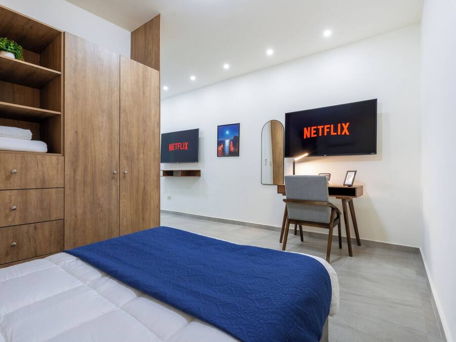 Habitación de hotel moderna con cama, armario de madera, escritorio y dos televisores grandes mostrando el logotipo de Netflix.
