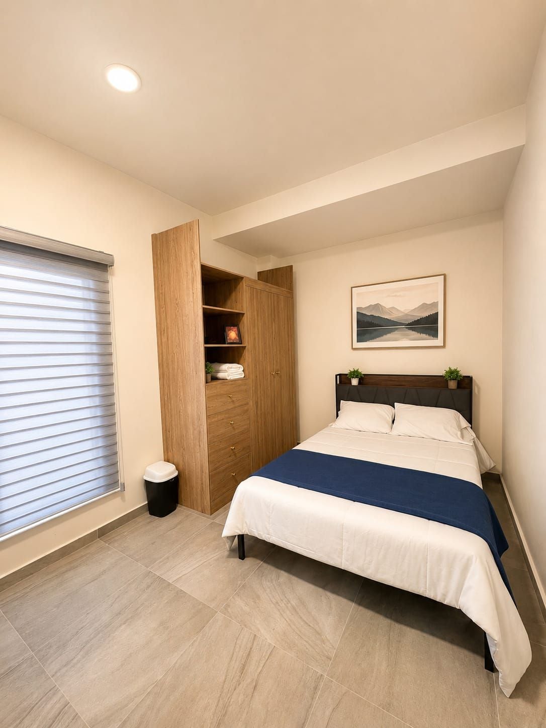 Un dormitorio con una cama, un armario de madera, un cuadro en la pared y una ventana con persianas.
