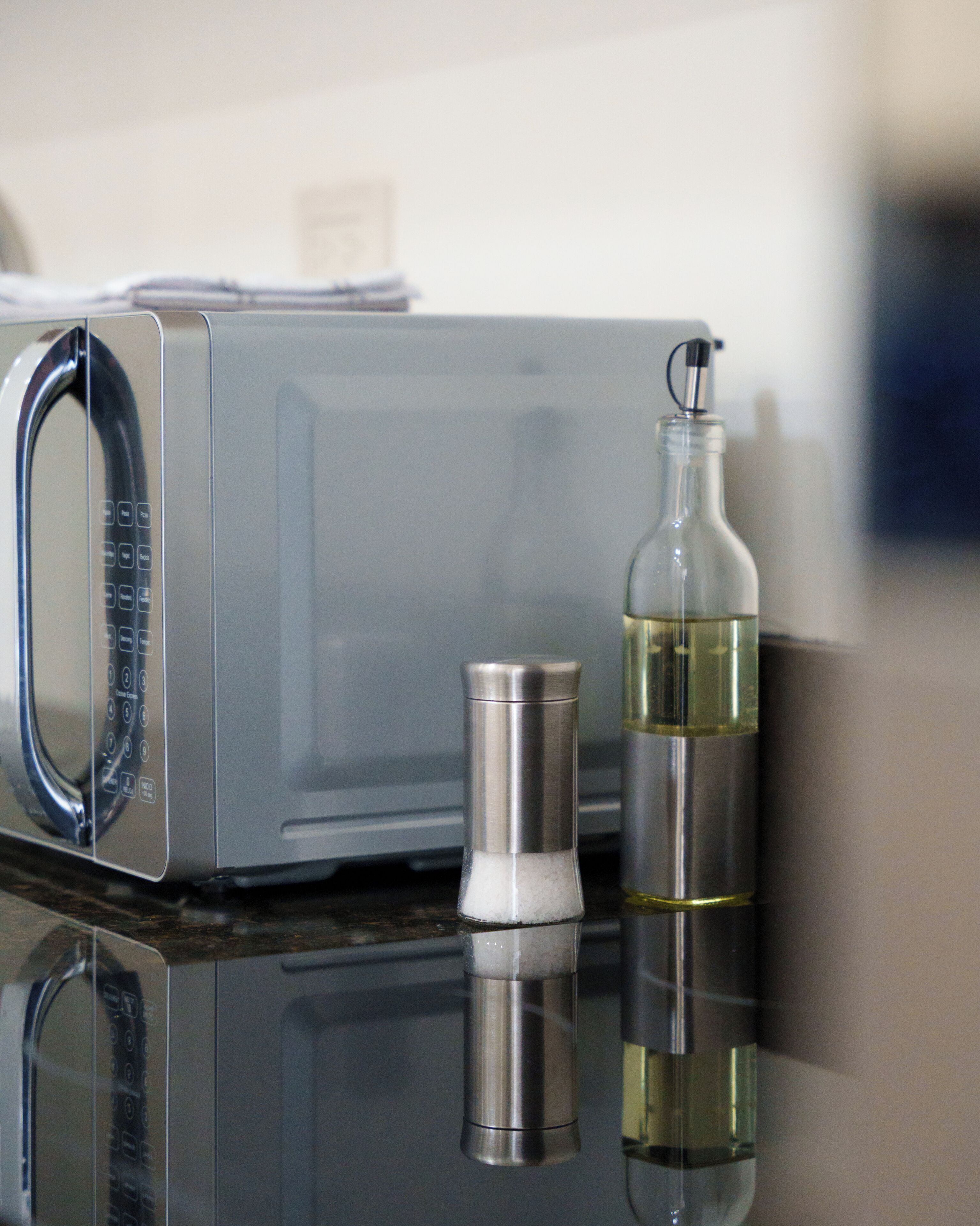Una cocina con microondas, salero y una botella de aceite sobre una superficie reflectante.