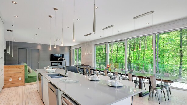 Una cocina moderna con una isla grande, comedor y ventanas amplias con vistas a un bosque.