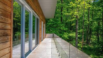 A wooden deck with glass railings overlooking a forested area.