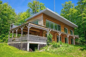 Ein modernes Holzhaus mit einer großen Terrasse, umgeben von üppiger Vegetation.