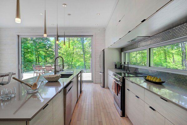 Une cuisine moderne dotée d’un grand îlot central, offrant une vue sur la verdure, et d’un coin repas avec des chaises.