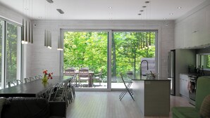 Una cocina moderna con una isla grande, una zona de comedor con sillas y vistas a la vegetación a través de amplios ventanales.