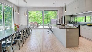 Cocina moderna con una isla grande, comedor con sillas y ventanas amplias con vistas a zonas verdes.
