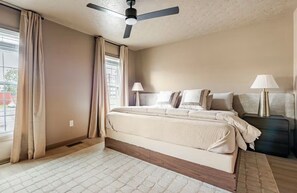 Une chambre à coucher avec un lit, deux lampes de chevet, un ventilateur de plafond et une fenêtre avec des rideaux.