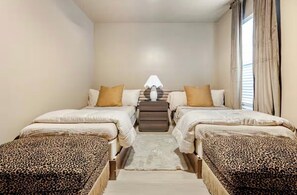 A bedroom with two beds, a nightstand, a lamp, and a view of the outside through a window. - River View Townhome w/ Balcony • 2BR • Sleeps 6 (Jeffersonville)