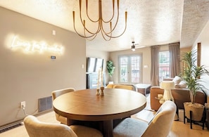 Un espace repas moderne avec une table ronde, des chaises, un lustre et un néon mural.