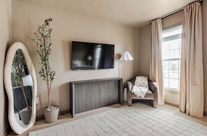 A living room with a TV, a sofa, a lamp, and a window with curtains. - River View Townhome w/ Balcony • 2BR • Sleeps 6 (Jeffersonville)