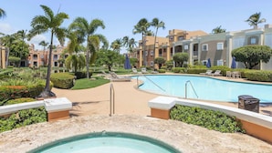 A pool area with lounge chairs, palm trees, and a building with balconies. - Fairway Courts Luxury Studio (FC872B) (Humacao)