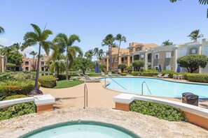 A pool area with lounge chairs, palm trees, and a building with balconies. - Fairway Courts Luxury Studio (FC872B) (Humacao)