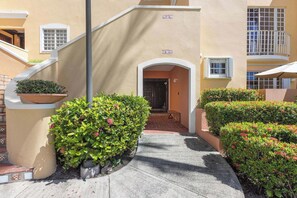A building entrance with a staircase, a door, and a small patio area with potted plants and a table. - Fairway Courts Luxury Studio (FC872B) (Humacao)