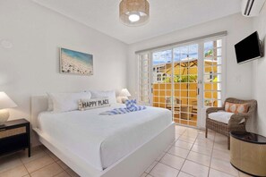 Ein Schlafzimmer mit Bett, Fernseher, Korbsessel und einem Balkon mit Blick.