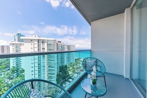 Ein Balkon mit zwei Stühlen und einem Tisch, mit Blick auf eine Stadtlandschaft und das Meer.