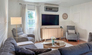 Una sala de estar con un sofá, sillones, una mesa de centro, un televisor y un reloj.